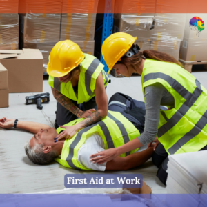 Two workers wearing yellow high-visibility vests and hard hats are providing first aid to a colleague who is lying on the ground in a warehouse. The injured person, also wearing a high-visibility vest, appears conscious as the workers attend to them. The scene is set among boxes and pallets, with a drill and a hard hat on the floor nearby. The NextGen Learning logo is displayed in the top right corner of the image. Below the scene is a text overlay that reads: "First Aid at Work" in a blue bar.