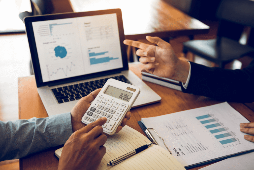 Business meeting with laptop charts, calculator, and printed reports showing financial data for cost control and management process
