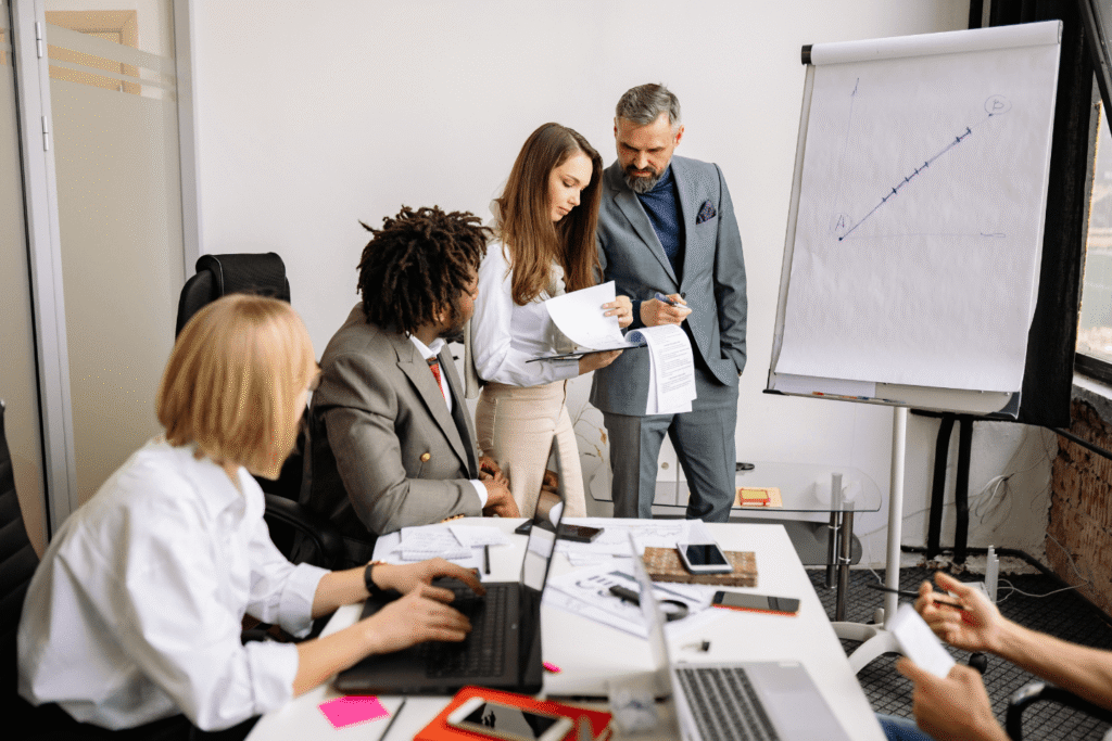 Modern office meeting with team analyzing data, reviewing strategy documents, and discussing customer acquisition selling strategies
